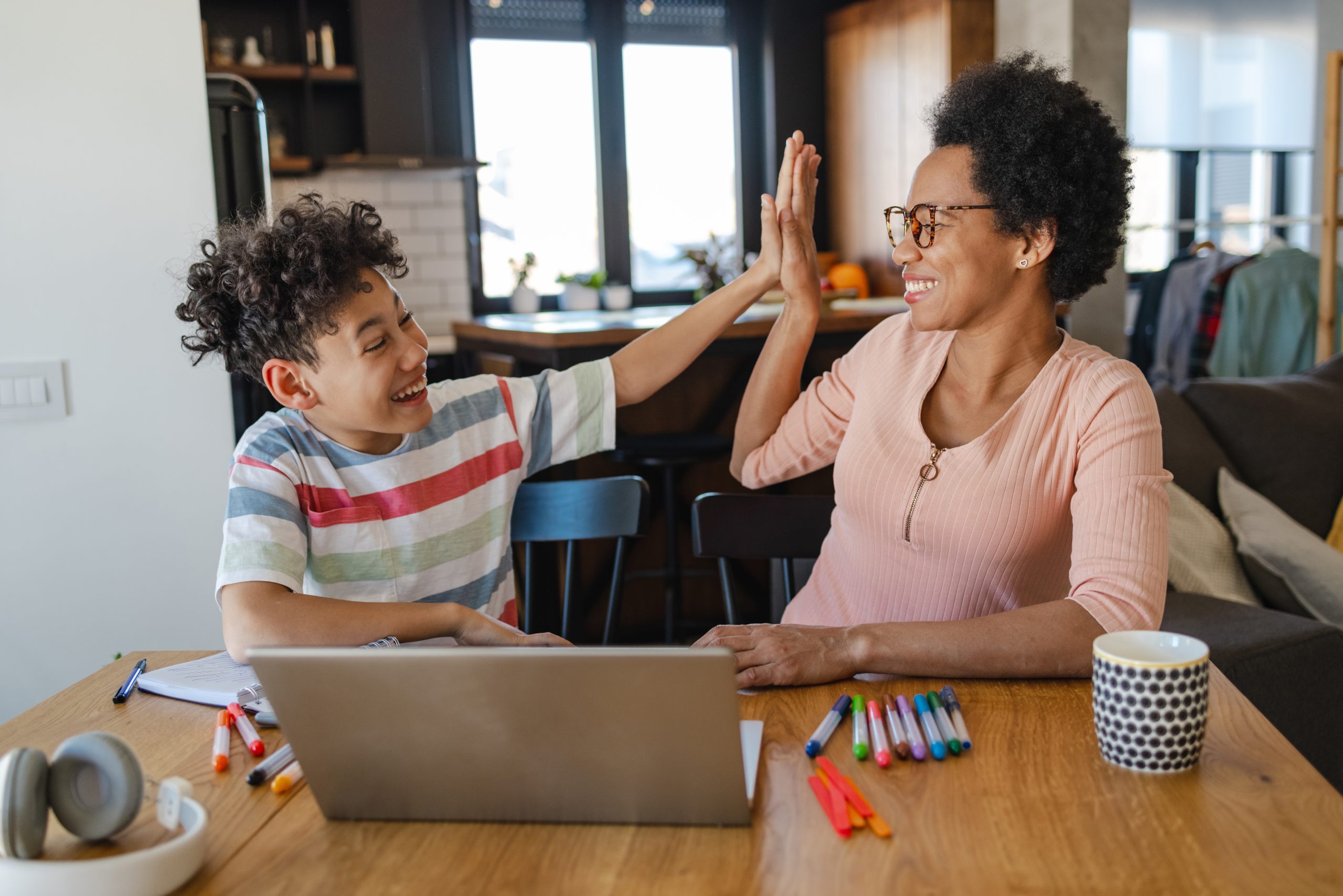 African-American mother and her son sitting at the table and using a laptop. They are happy and cheerful