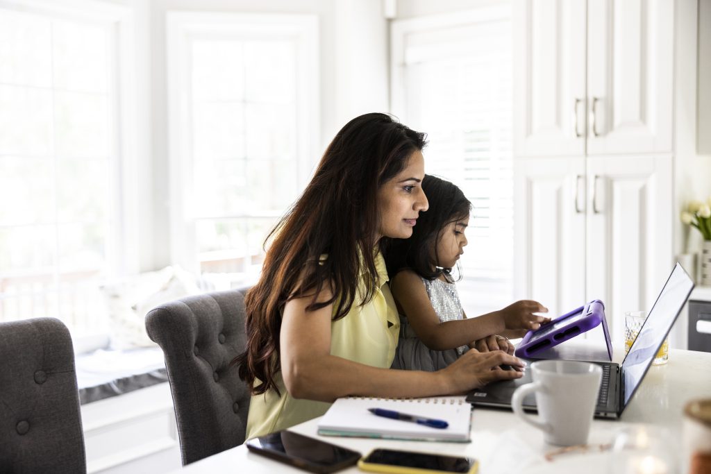 Mother using laptop and smartphone while holding toddler daughter
