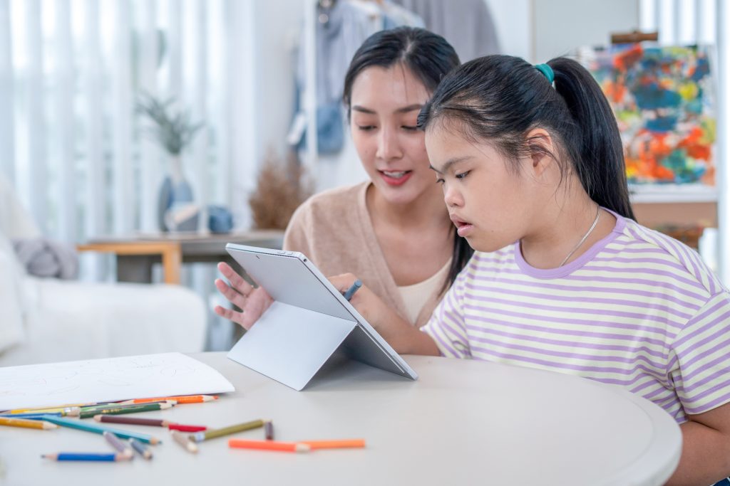 Teacher teaching an autistic girl student to use an E-learning program from a tablet.