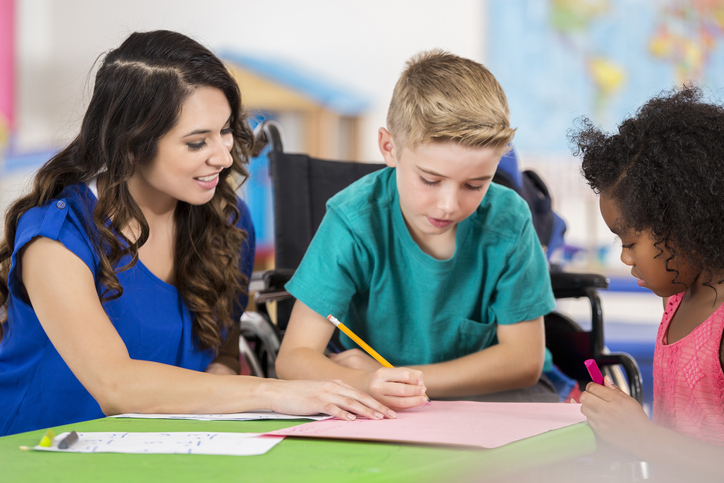 Teacher helping an elementary age boy in a wheelchair with schoolwork